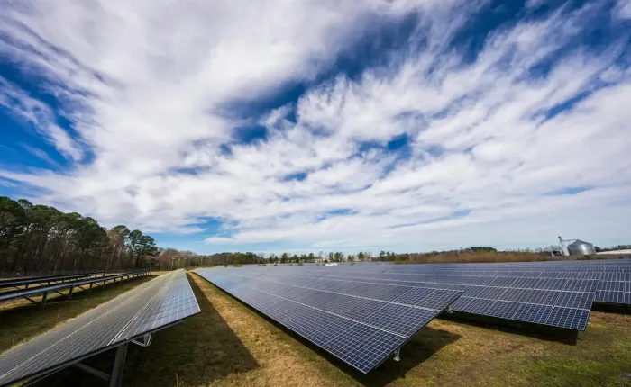 Huerto de placas solares, el cielo esta algo nublado, de fondo hay árboles.